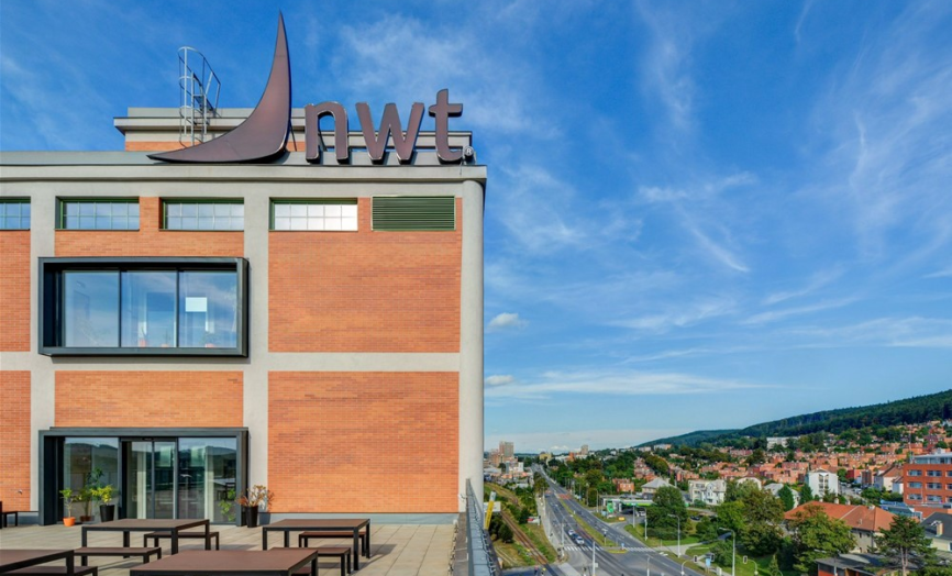 Budova společnosti NWT s výrazným logem na střeše a výhledem na město a okolní krajinu.